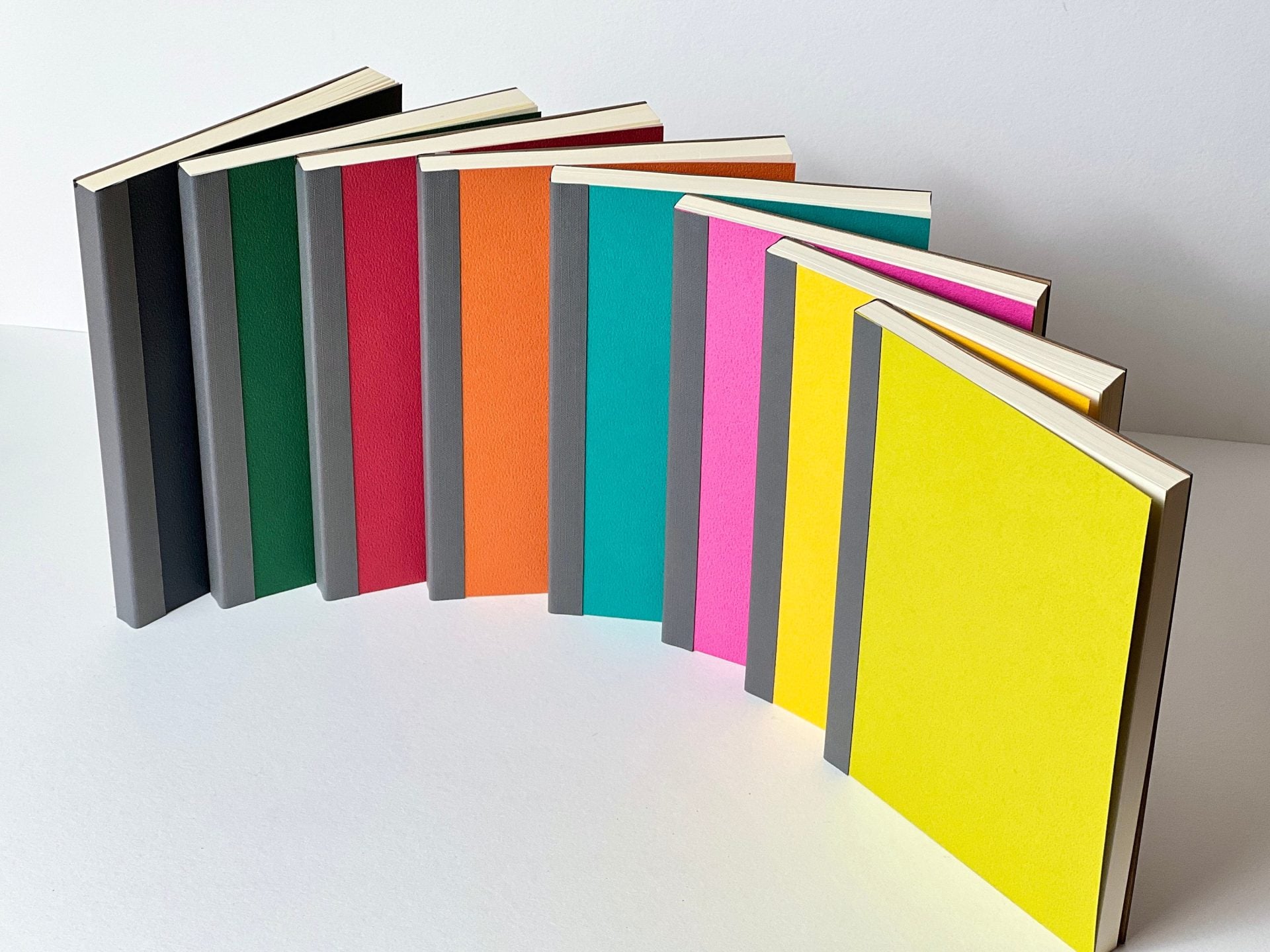 A collection of colorful notebooks laid out next to each other in a gradient of colors, ranging from yellow, green, blue, red, to black.
