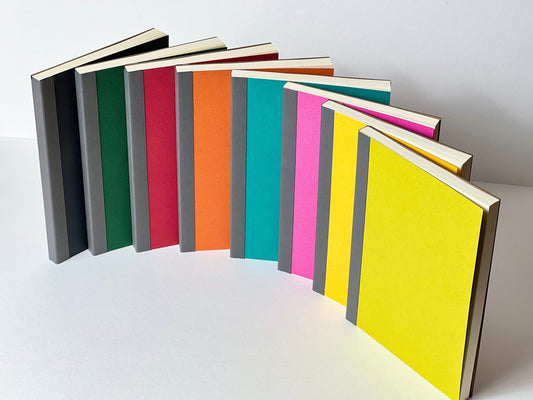 A collection of colorful notebooks laid out next to each other in a gradient of colors, ranging from yellow, green, blue, red, to black.